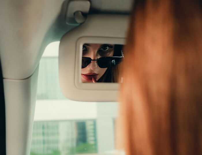 Woman with sunglasses applying lipstick in a truck mirror, capturing truckers share craziest things seen moment. - 29