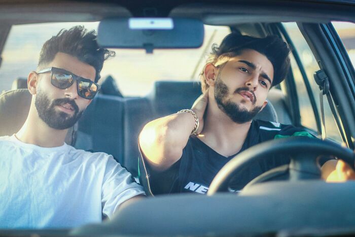 Two young men sitting in a car, one wearing sunglasses, both showing pensive expressions, reflecting breakup emotions.