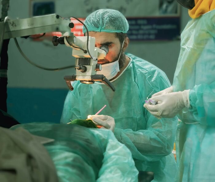 Scientist in surgical attire using a microscope to carefully study bodies donated to science in a clinical setting