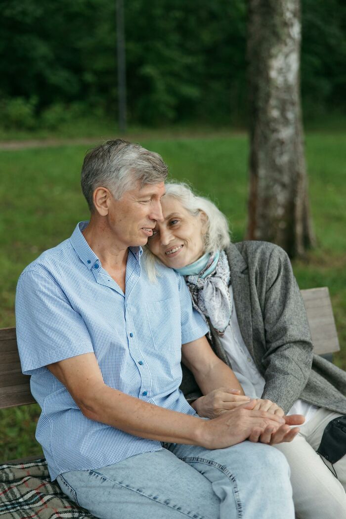 Older couple sitting on a bench outdoors, sharing a tender moment reflecting life after divorce for older people. - 31