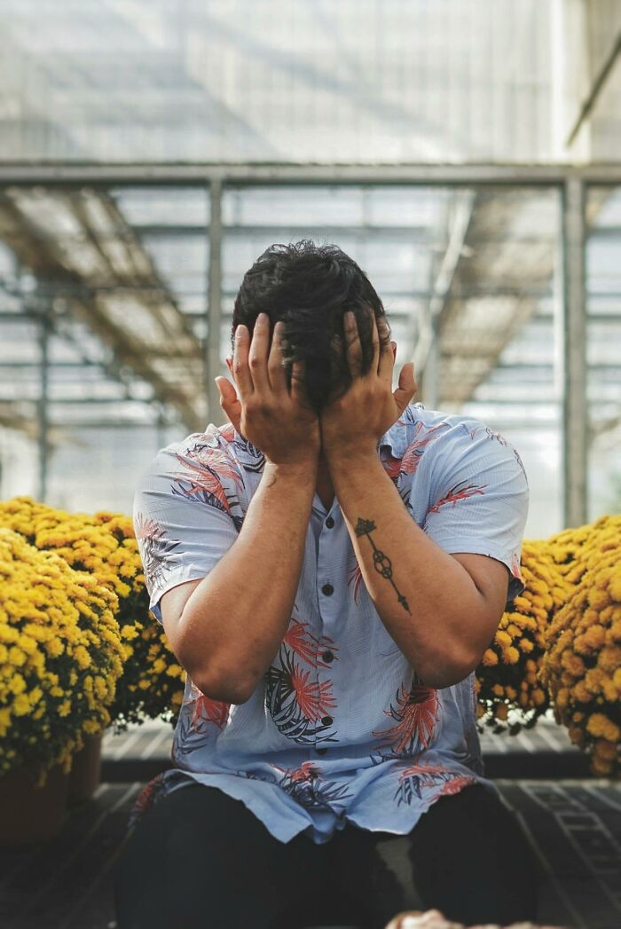 Man covering his face in distress sitting among yellow flowers, illustrating disturbing things people overheard someone say.