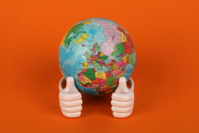Globe held by two thumbs-up hands on an orange background symbolizing geography buff challenge with emoji combos.