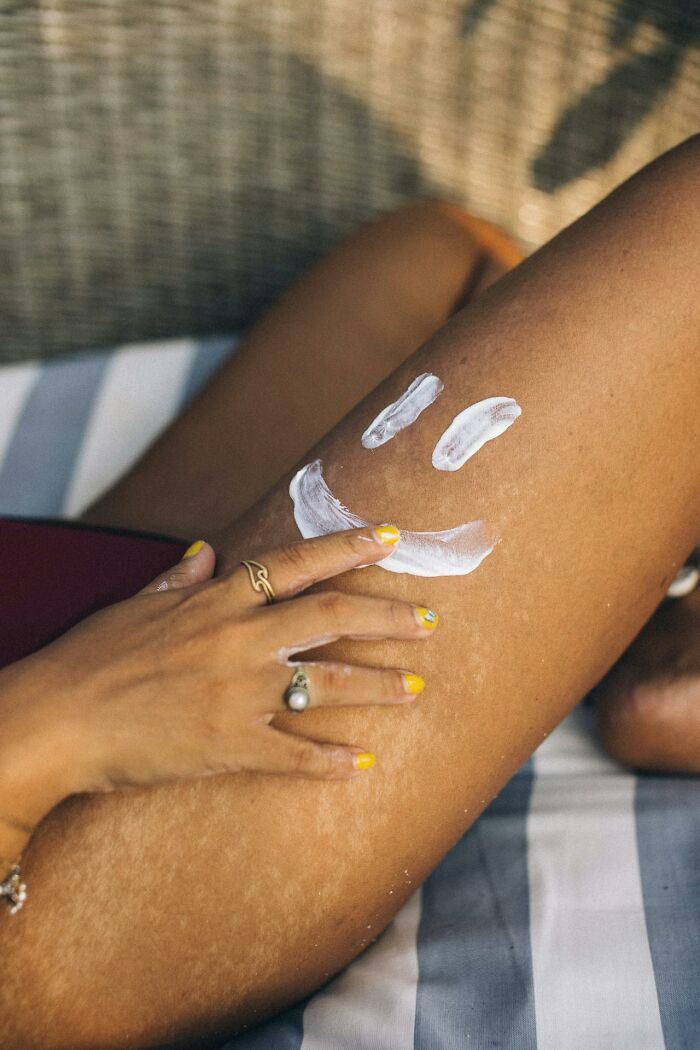 Hand with rings applying sunscreen lotion with smiley face on leg, illustrating survival tips for skin protection.
