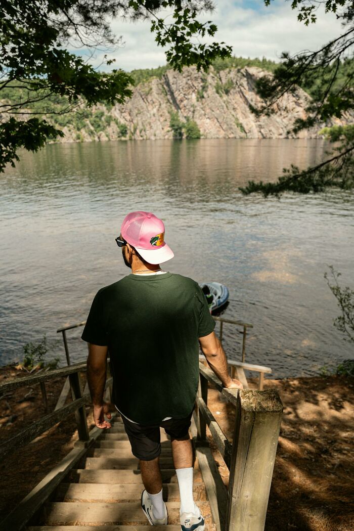 Man in a pink cap walking down wooden stairs toward water, illustrating survival tips in an outdoor natural setting.