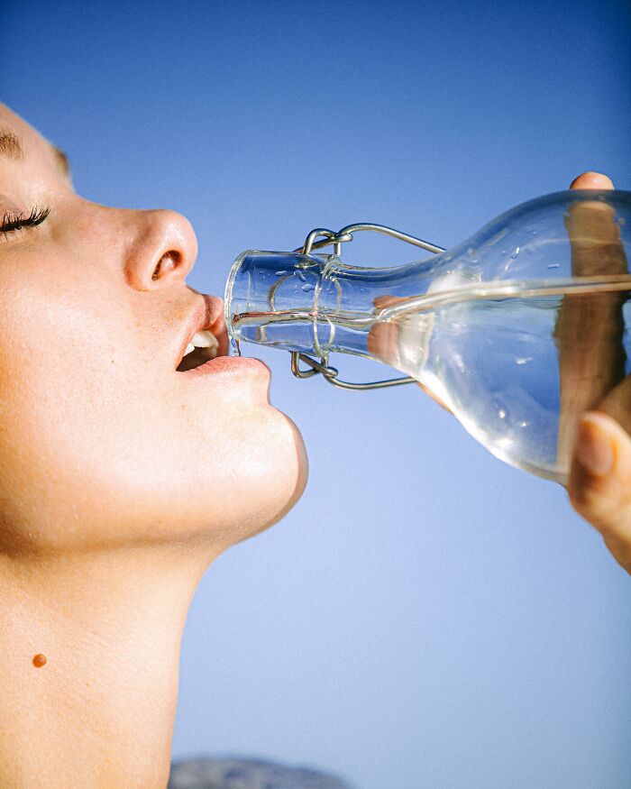 Close-up of a woman drinking water from a glass bottle outdoors, illustrating gut feeling moments that saved lives.