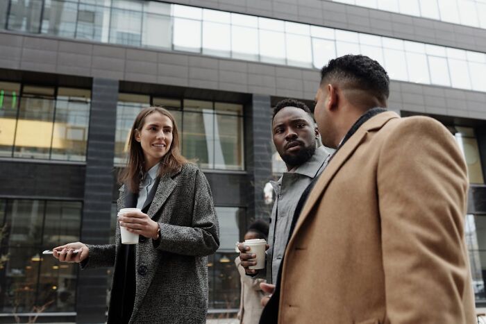 Three professionals having coffee outside a modern office building, discussing ways to take revenge on their bosses. - 21
