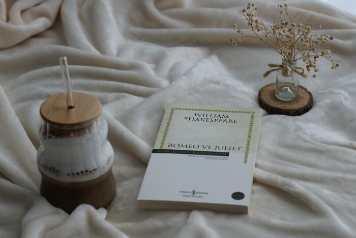 Soft cozy setting with Romeo and Juliet book, dried flowers, and a drink, illustrating romanticized red flags in relationships. - 3