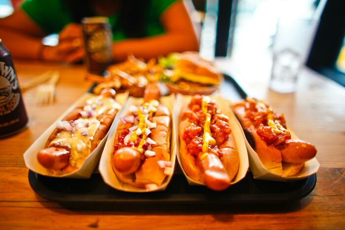 Four gourmet hot dogs with various toppings on a tray, illustrating harmless lies parents told that left netizens low key traumatized. - 5
