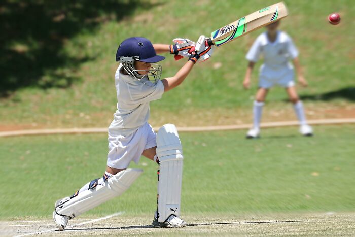 Young cricket player in white gear hitting the ball during a match on a sunny field, illustrating teamwork and sportsmanship.