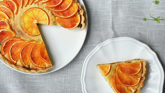 Orange tart with slices arranged in a circle on a white plate, with a single slice served on a separate plate, pickup lines concept.