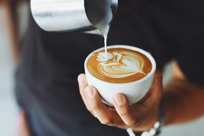 Person pouring steamed milk into coffee cup creating latte art, illustrating warm and creative pickup lines.