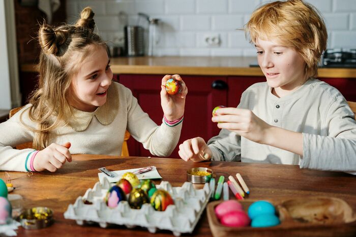 Two children painting colorful eggs at a table, illustrating creativity linked to outrageous student names shared by a teacher.