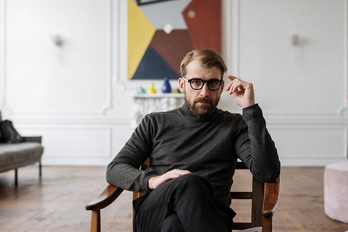Man with glasses sitting thoughtfully in a modern room, representing people who had enough of their partner's shenanigans.
