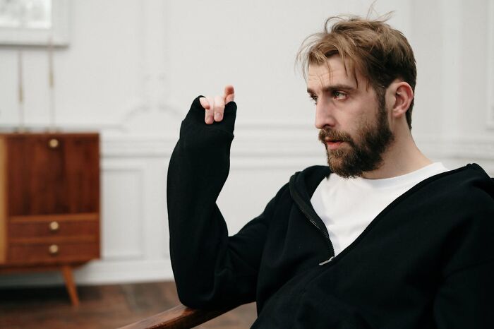 A frustrated man with a beard wearing a black hoodie, gesturing while expressing entitlement in a casual indoor setting.