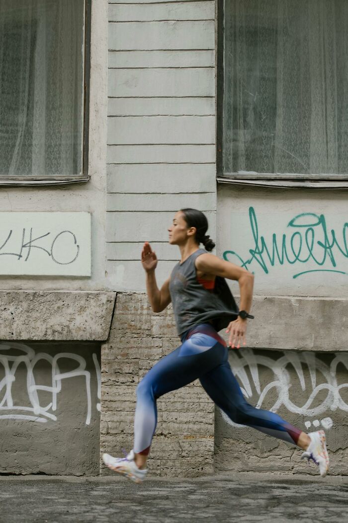 Woman in athletic wear running beside a graffiti-covered wall illustrating survival tips in an urban setting