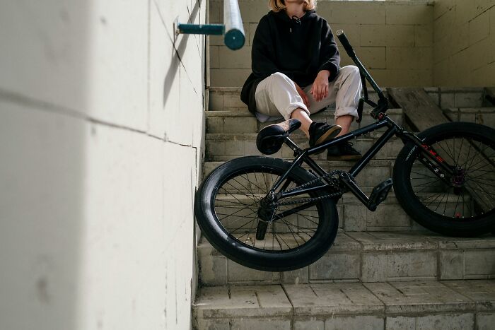 Person sitting on indoor stairs with a BMX bike, wearing casual clothes in a dimly lit stairwell setting, symbolizing pickup lines.
