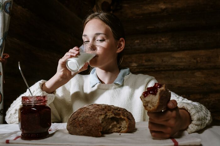 Person drinking milk and eating bread with jam in a rustic setting, illustrating things non-Americans do that confuse Americans. - 32