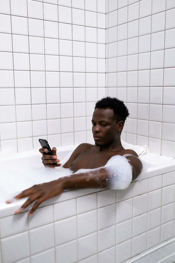Man in bathtub with soap bubbles checking phone, illustrating cheating red flags and relationship trust issues. - 18
