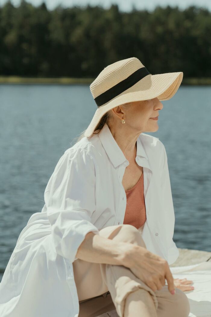 Older woman relaxing by the water wearing a sunhat, reflecting on life after divorce in her senior years. - 16