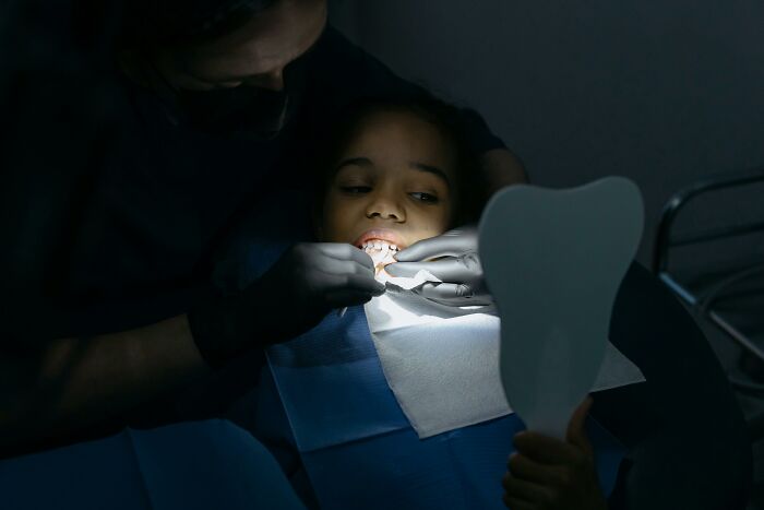 Child at dentist receiving treatment, holding a mirror, highlighting harmless lies from parents that caused low key trauma. - 26
