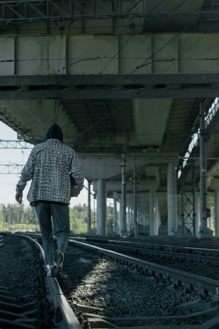 Person in a hooded jacket walking on railroad tracks under a bridge, illustrating survival tips concept.