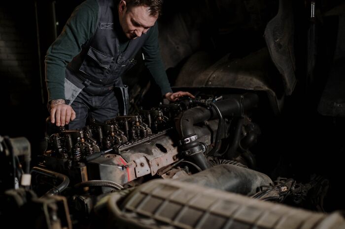 Mechanic inspecting engine in dimly lit garage, representing one of the six-figure jobs that don’t get enough credit.