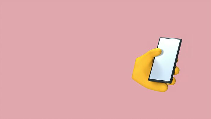 Yellow emoji hand holding a smartphone against a pink background for geography buff emoji country decoding. Yellow emoji hand holding a smartphone against a pink background for geography buff emoji country decoding.