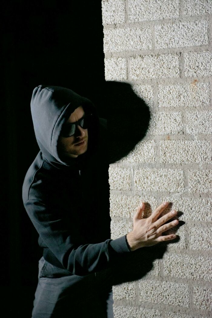 Person in a dark hoodie and sunglasses hiding behind a brick wall, symbolizing toxic behavior in friendships. - 50