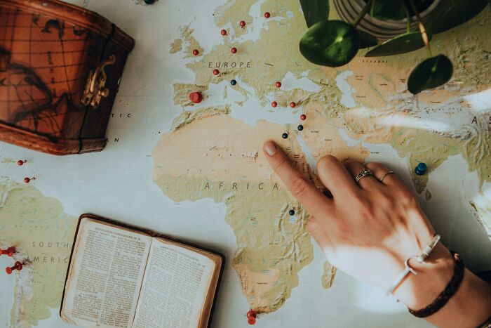 Person pointing at a map of Africa with pins, an open book, and a vintage leather suitcase nearby, exploring history and geography. Person pointing at a map of Africa with pins, an open book, and a vintage leather suitcase nearby, exploring history and geography.