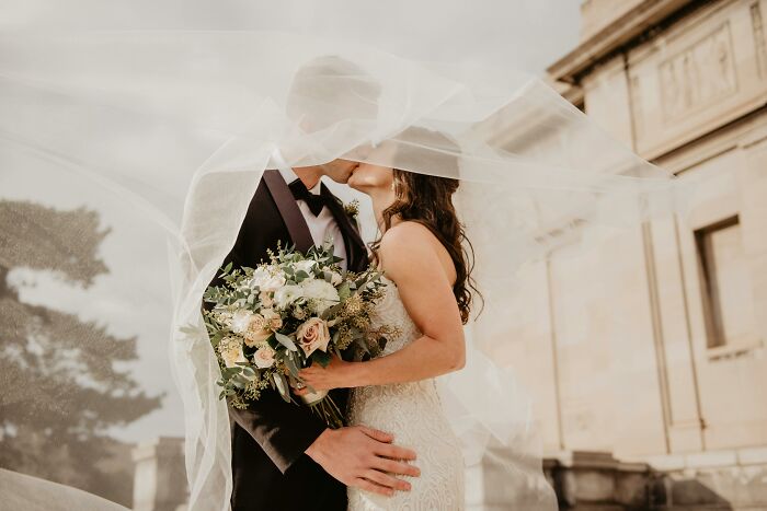 Bride and groom sharing a kiss under a flowing veil, symbolizing romance with hidden red flag relationship signs. - 5