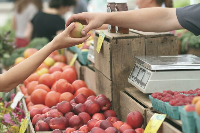 Hand exchanging fresh fruit at market, highlighting food waste crisis and the global problem of wasted food resources.