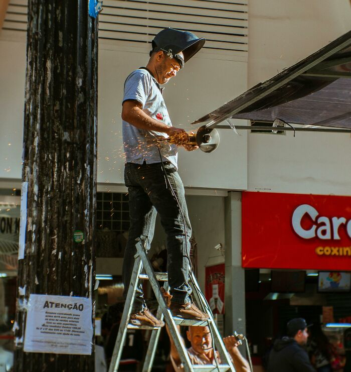 Trabajador en escalera usando equipo de protección mientras corta metal, ilustrando secretos que las empresas ocultan a clientes.