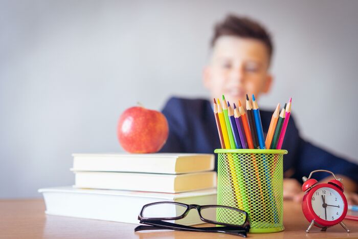 Colorful pencils in a holder with books, apple, glasses, and a red clock on desk, symbolizing smarter than a high schooler challenge. Colorful pencils in a holder with books, apple, glasses, and a red clock on desk, symbolizing smarter than a high schooler challenge.