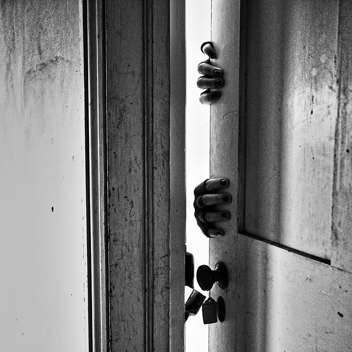 Hands gripping a slightly open door, creating a mysterious atmosphere related to neighbor tales in a quiet woods setting.