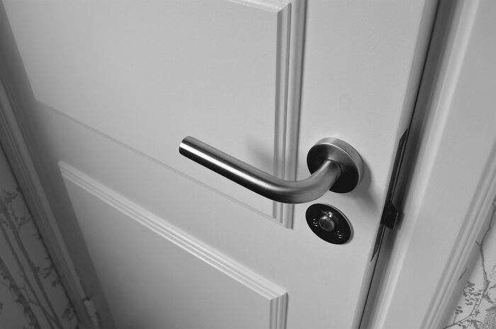 Close-up of a silver door handle on a white door, symbolizing petty things in breakups and borderline insane actions.