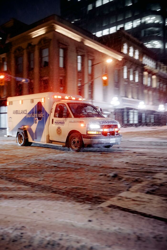 Ambulance with flashing lights driving through snowy urban street at night, highlighting emergency medical response for patients.