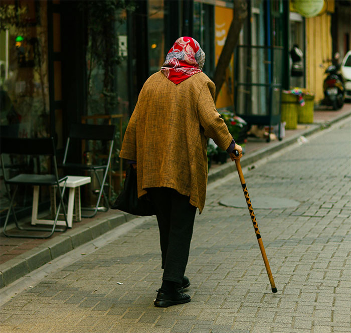 An elderly person walking on a city street with a cane, illustrating stories from people who deal with dead bodies.