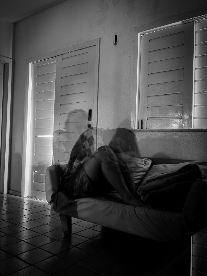 Person sitting on a couch in a dim room with blurred motion, evoking eerie neighbor tales and a desire to move to the woods.