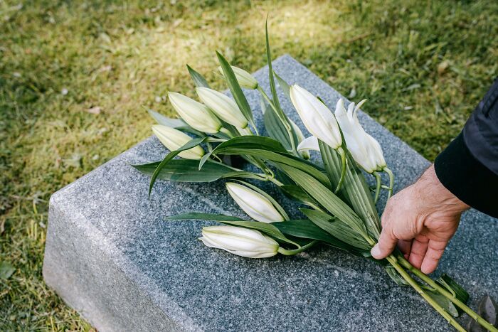 A hand placing white lilies on a granite grave, reflecting moments people who deal with dead bodies experience.