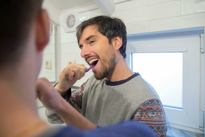 Man brushing teeth in bathroom mirror, illustrating pettiest things in breakups with borderline insane behavior.