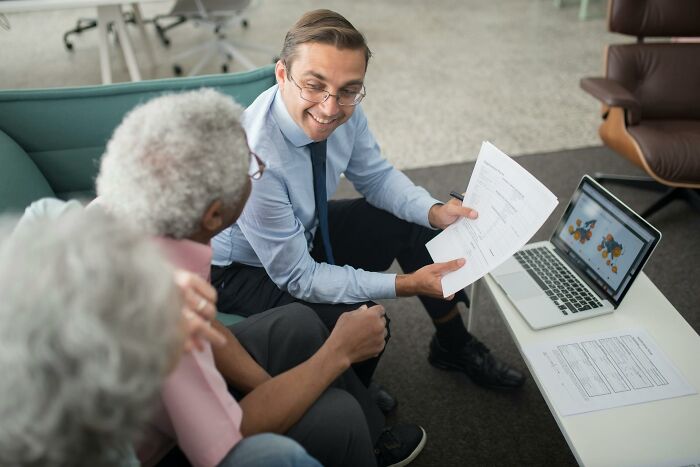 Man in business attire reviewing job options on paper and laptop with two older adults discussing six figure jobs.