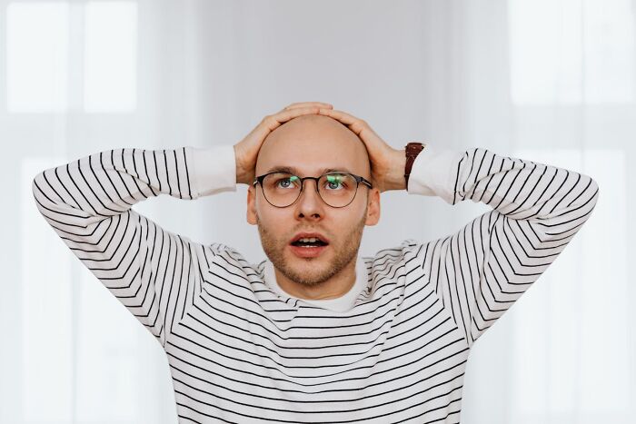 Man wearing glasses and striped shirt looking shocked with hands on head, illustrating disturbing things overheard.