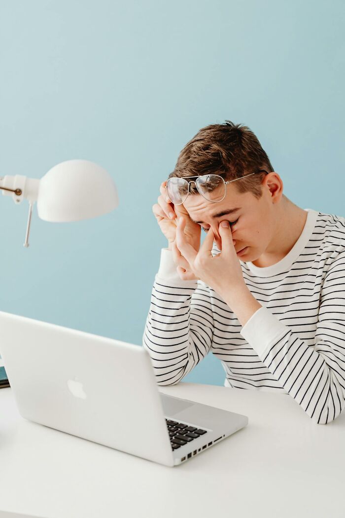 Young man in striped shirt rubbing his eyes in front of a laptop, representing entitled patients demanding special treatment.