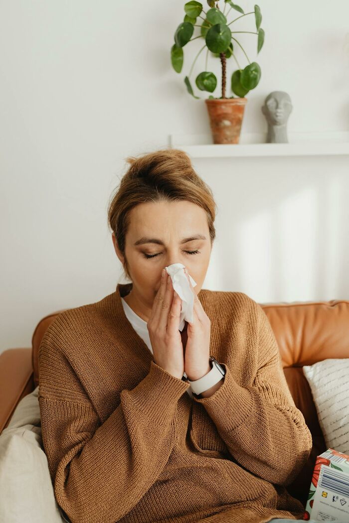 Woman in brown sweater blowing her nose while sitting indoors, related to survival tips that won't help you.