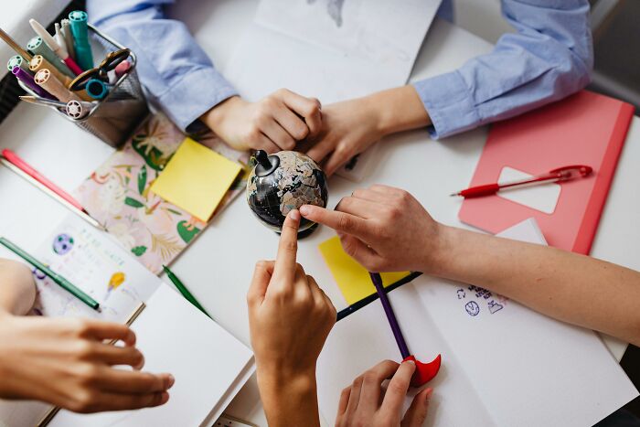 Hands pointing at a small globe on a desk with papers and pens, highlighting a geography odd one out quiz theme.