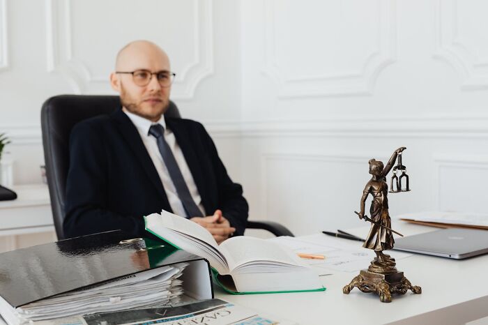 Man in a suit at office desk with legal books and Lady Justice statue, representing high paying jobs with six figures.