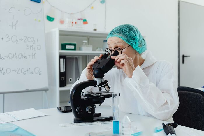 Scientist wearing protective gear using a microscope in a lab, studying bodies donated for science research.