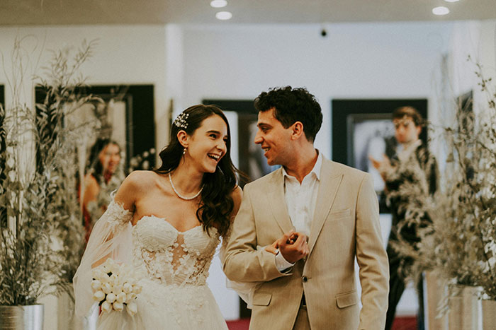 Bride and groom smiling at wedding ceremony, with guests in background, capturing best man&rsquo;s speech moment.