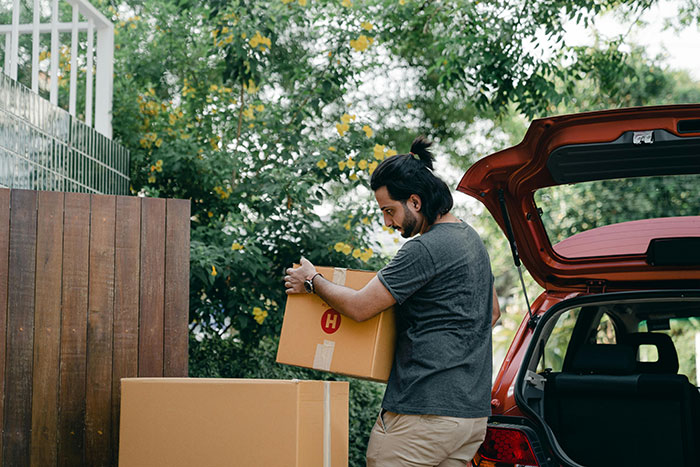 Man lifting a cardboard box outdoors near a car, symbolizing tension in a manipulative mom daughter story drama. - 44