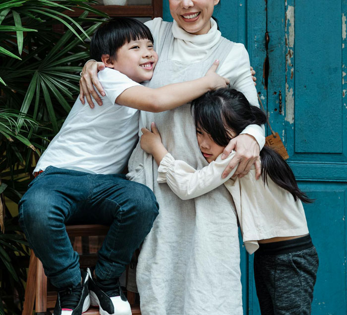 Young boy hugs mother smiling while girl clings sadly, illustrating golden child stealing brother&rsquo;s gifts conflict.